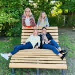 Vier Frauen entspannen auf großer Parkbank draußen