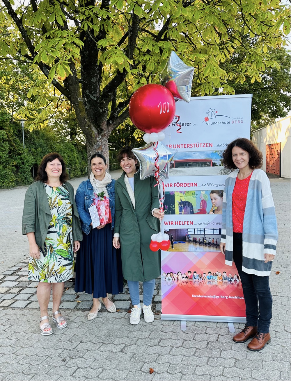 Frauen stehen mit Ballons vor Werbebanner draußen