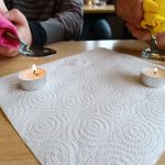 Zwei brennende Teelichter neben Löffeln und Servietten