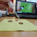 Hand mit Pipette tropft Wasser auf Münzen