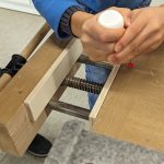 Person bearbeitet Holz mit Schraubzwingen und Leim