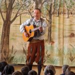 Mann spielt Gitarre vor einer Kindergruppe.