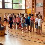 Kinder stehen in einer Turnhalle in Reihe
