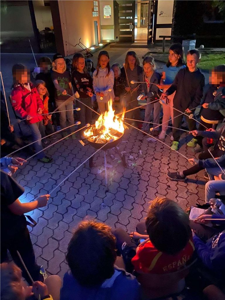 Kinder genießen Lagerfeuerabend mit Marshmallows draußen