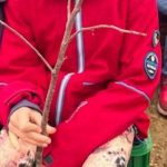 Kind mit roter Jacke und Zweig draußen